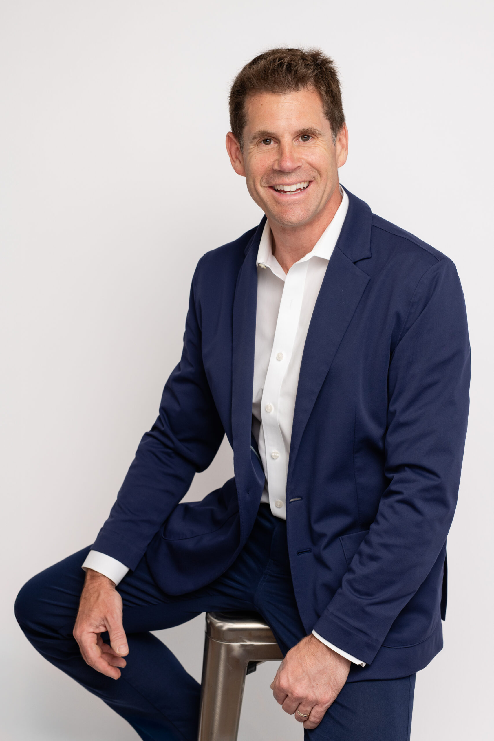 Man in navy suit smiling, professional headshot.
