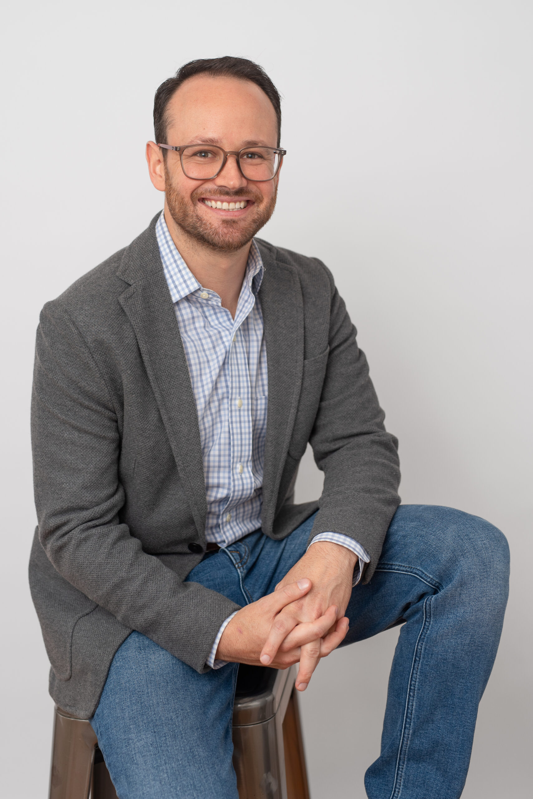 Man in gray blazer with glasses, smiling headshot.