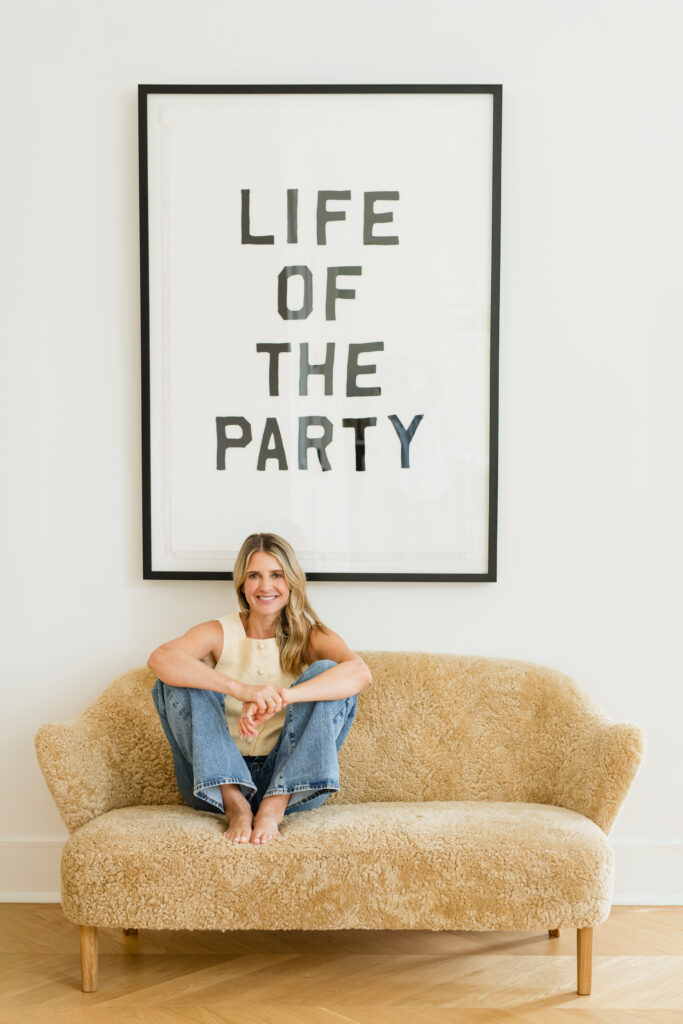 Woman on sofa with “Life of the Party” sign, casual portrait.