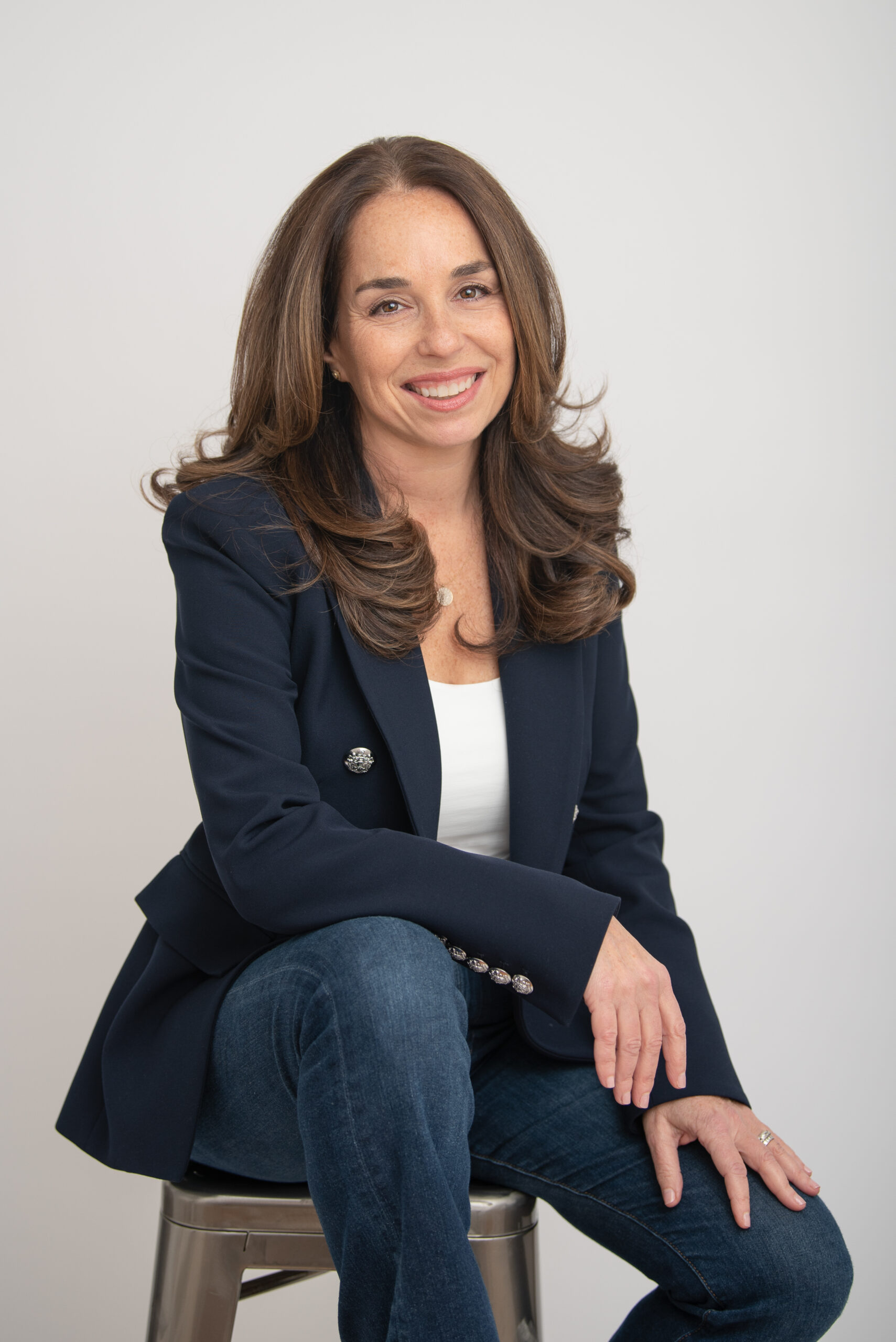 Woman in navy blazer, seated and smiling headshot.