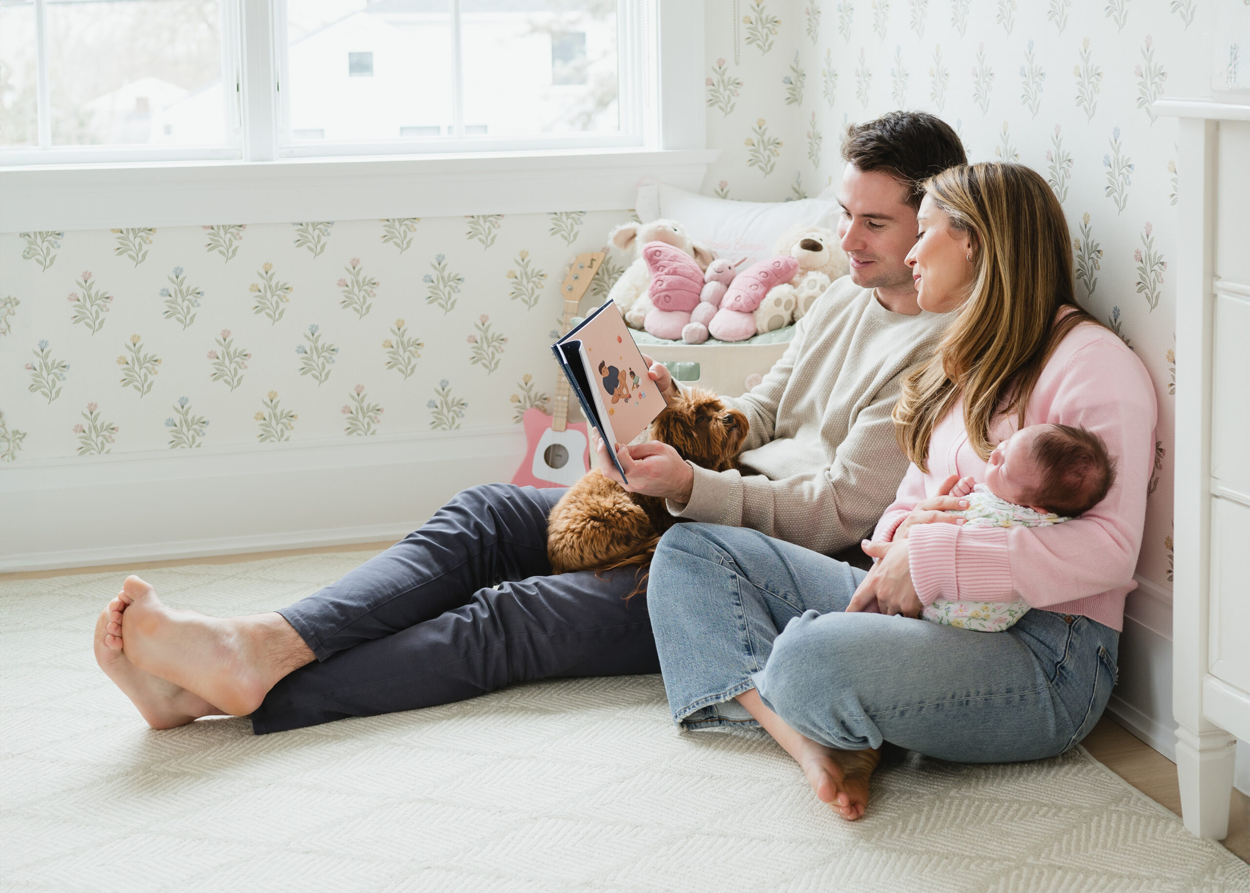first time parents snuggling together in the nursery with baby and family dog 
